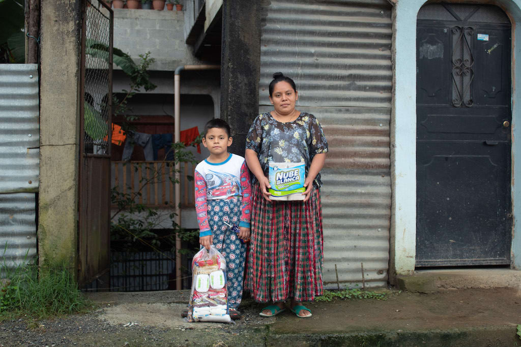 A mother and son stand together holding bags of supplies.
